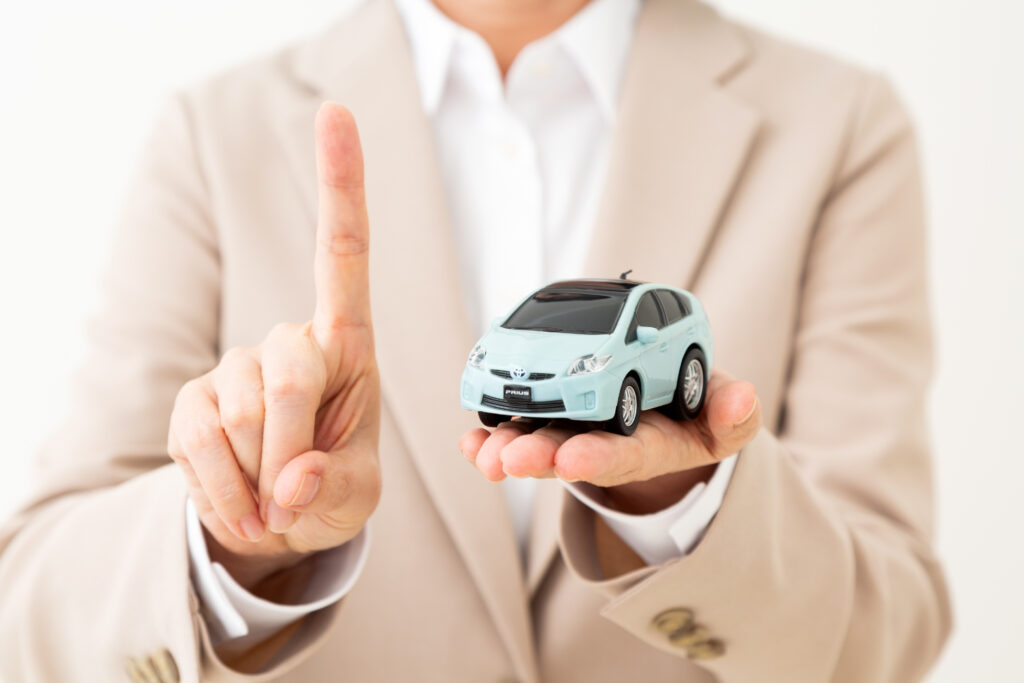 車の模型を持って人差し指を立てるスーツ姿の女性