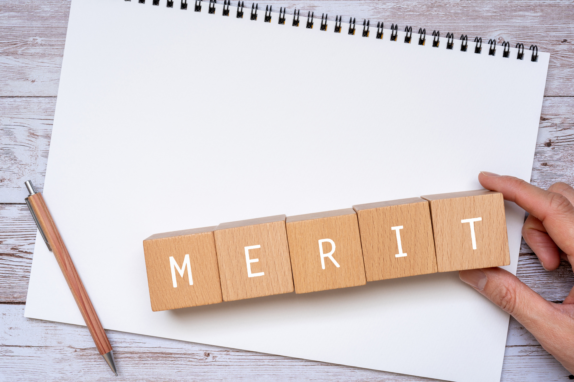 「MERIT」と書かれた積み木、ノート、ペン、人の手
