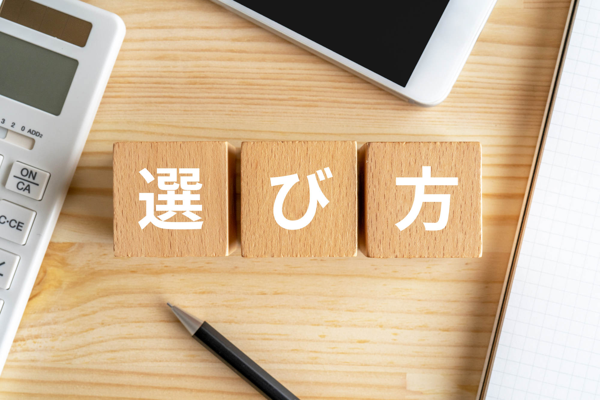 選び方と書かれたブロック、電卓、スマホ、ノート
