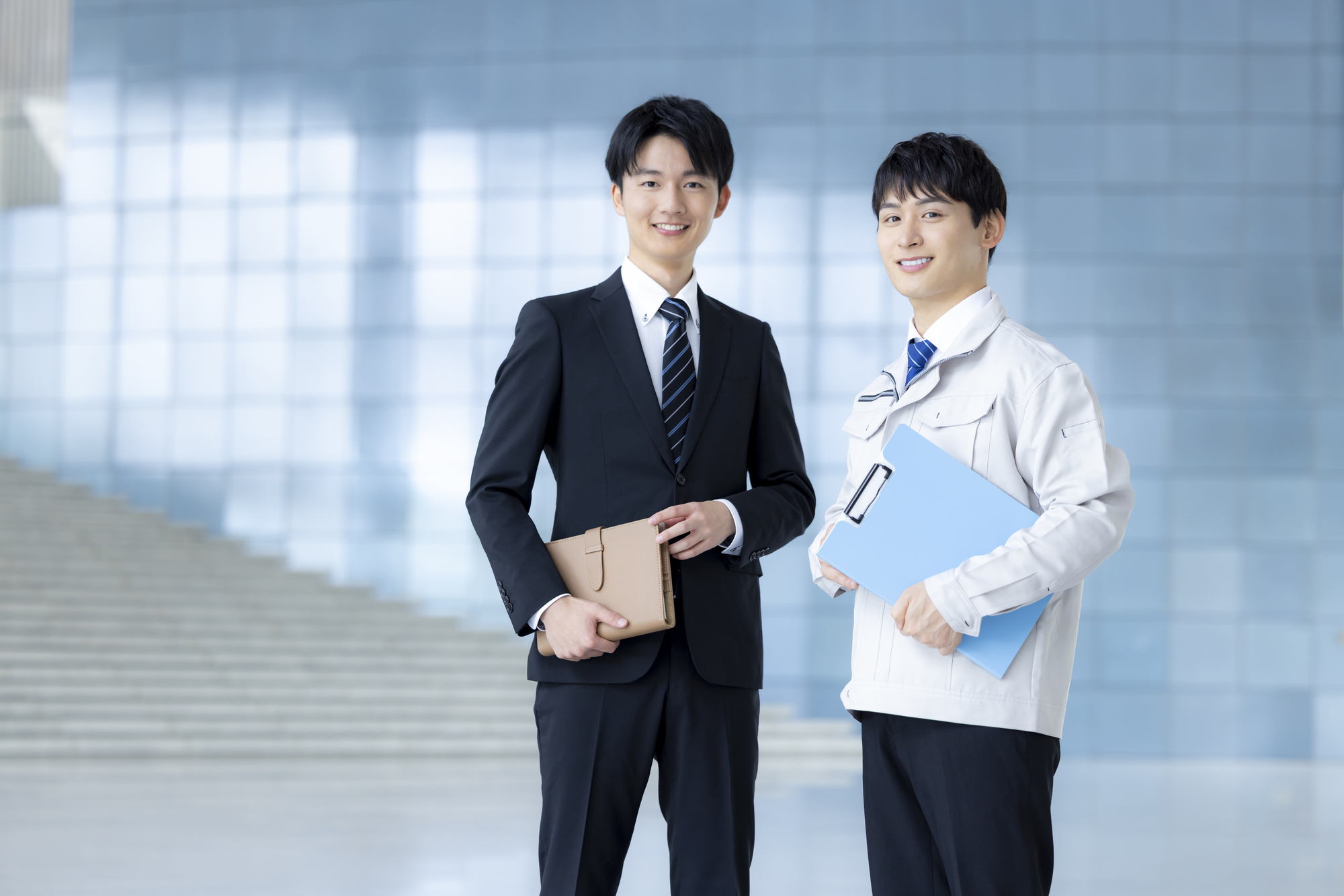 スーツを着た男性と作業着を着た男性・いずれも笑顔